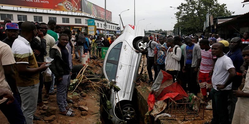People look at a car in a sewer after a flood in Abidjan