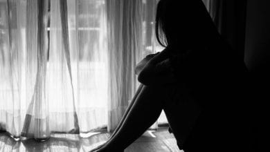black and white of sad woman hug her knee and cry. Sad woman sitting alone in a empty room beside window or door