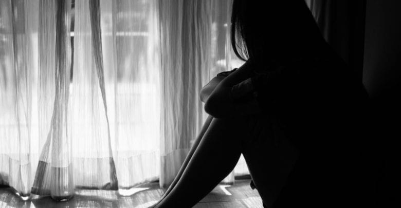 black and white of sad woman hug her knee and cry. Sad woman sitting alone in a empty room beside window or door