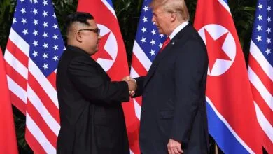 Donald Trump serrant la main de Kim Jong-un devant les drapeaux américain et nord-coréen